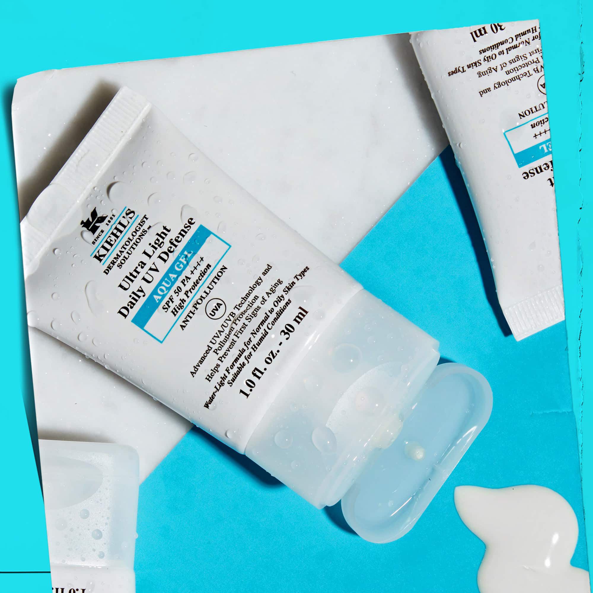 Ploche usporiadanie viacerych tub Ultra Light Daily UV Defense Aqua Gel na mramorovom povrchu, ukazujuce ich lifestylovy vzhľad.