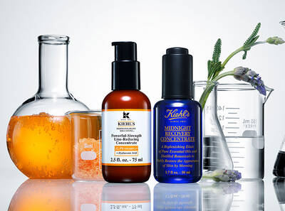 Rozne fľaštičky s kozmetickymi produktmi Kiehl's, obklopene meracimi nadobami a oranžovou kvapalinou.