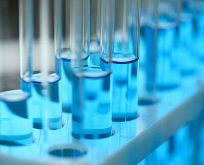 Close-up of several test tubes filled with blue liquid, placed in a test tube rack, with a soft blue glow illuminating the scene.