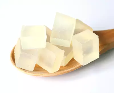 A wooden spoon holds several translucent, pale cubes of jelly-like substance.