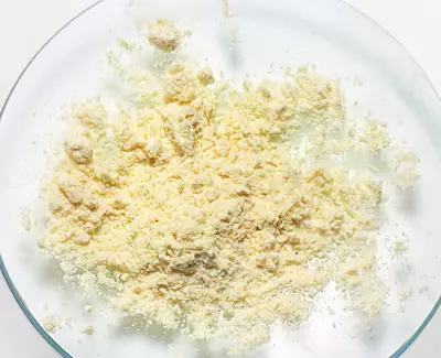 A clear glass dish containing a mound of light yellow, finely ground powder resting on a white background.