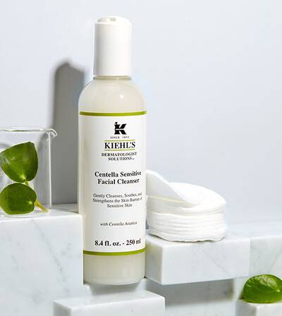 Čistiaci gel Kiehl's Centella Sensitive Facial Cleanser na citlivu pleť, umiestneny na mramorovej podložke s vatovymi tamponmi.