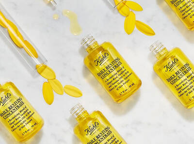 Fľaštičky s Kiehl's dennym revitalizačnym koncentratom na bielom pozadi, obklopene okvetnymi listkami a kvapkami oleja.