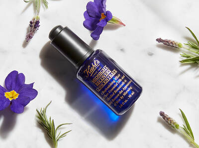 Modra fľaštička s pleťovym olejom na bielom pozadi, obklopena levanduľou a fialkami.
