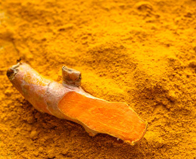 A piece of fresh turmeric root resting on a bed of bright yellow turmeric powder.