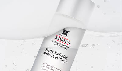 A bottle of Kiehl's Daily Refining Milk-Peel Toner, featuring a sleek design with white and silver colors, against a backdrop of flowing water.