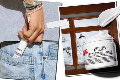 The image features a hand reaching into a denim pocket, holding a tube of Kiehl's Ultra Facial Cream, alongside an open jar of the cream and a window showing a snowy landscape outside.