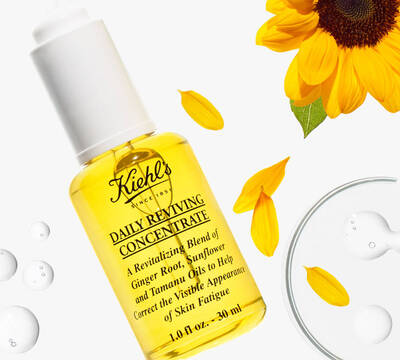 Žlte serum Kiehl's Daily Reviving Concentrate s olejom zazvoru a slnečnice na oživenie pleti, obklopene slnečnicovymi lupienkami.