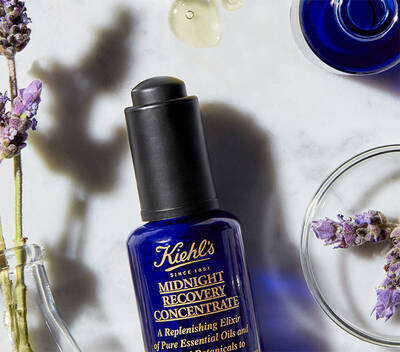 Fľaša s olejom Kiehl's Midnight Recovery Concentrate vedľa sušenych levanduľovych kvetov na mramorovej doske.