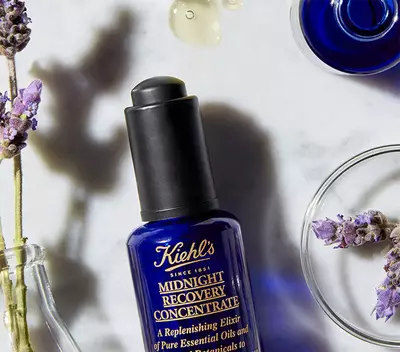Fľaša s olejom Kiehl's Midnight Recovery Concentrate vedľa sušenych levanduľovych kvetov na mramorovej doske.