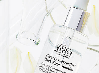Clear serum Kiehl's na odstranenie tmavych škvŕn s elegantnym obalom a bielymi kvetmi v pozadi.