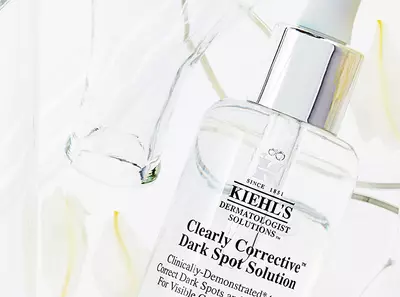 Clear serum Kiehl's na odstranenie tmavych škvŕn s elegantnym obalom a bielymi kvetmi v pozadi.