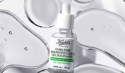 A dropper bottle of Kiehl's Ultra Pure High-Potency Serum with 5% Niacinamide, surrounded by scattered drops of clear liquid on a white background.
